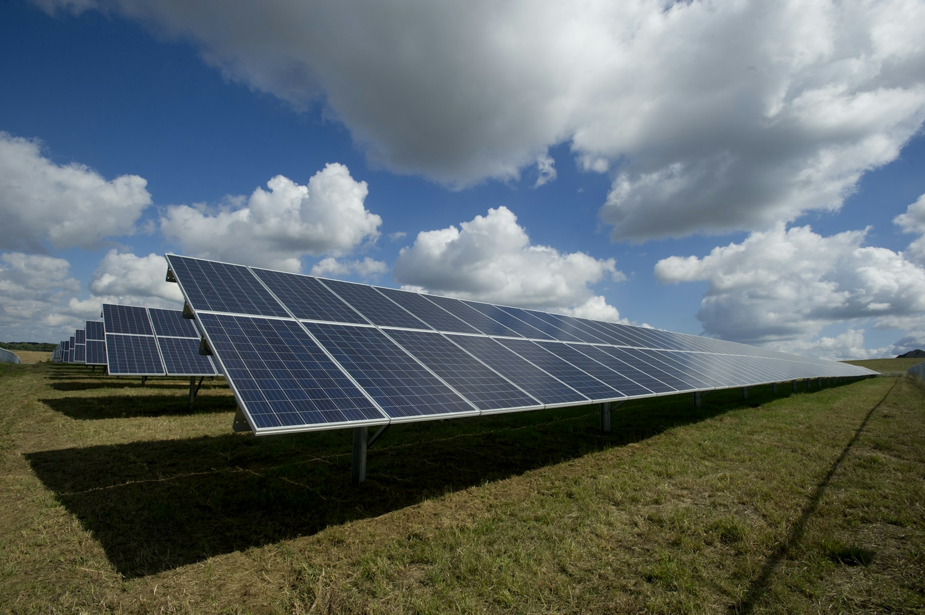 Reihen von Photovoltaikmodulen auf einer Freifläche unter bewölktem Himmel